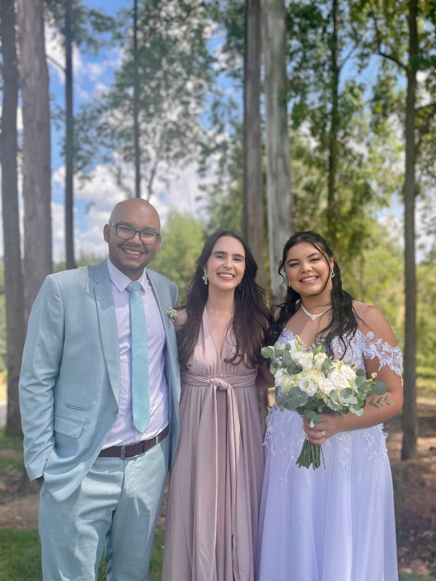 Giovana com casal de noivos entre as árvores