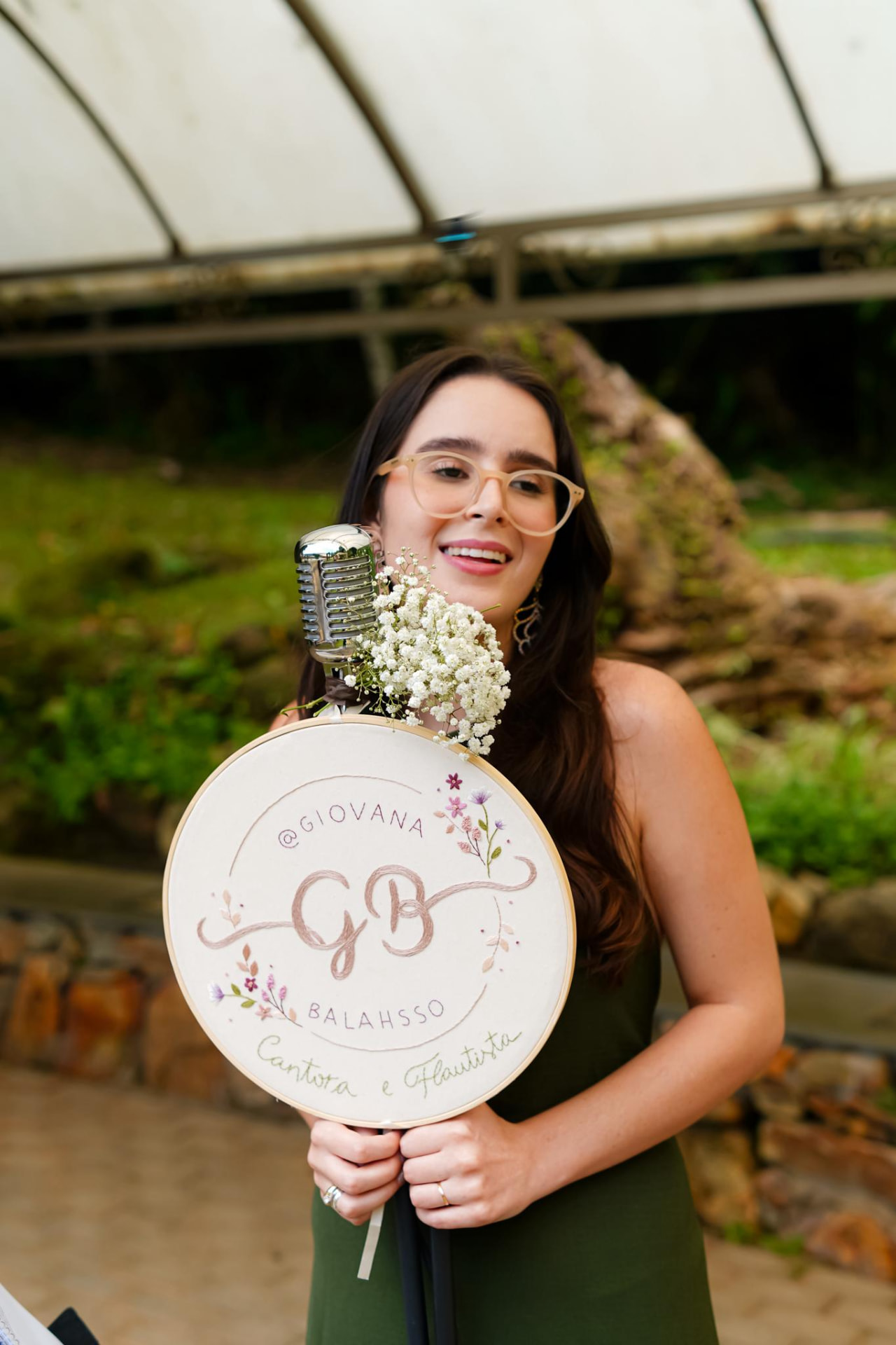 Giovana sorrindo com microfone vintage e bastidor bordado